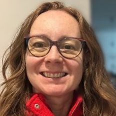 Photo of Cristina Chaplin-Rueda, who is a smily red-head with glasses and wearing a red coat